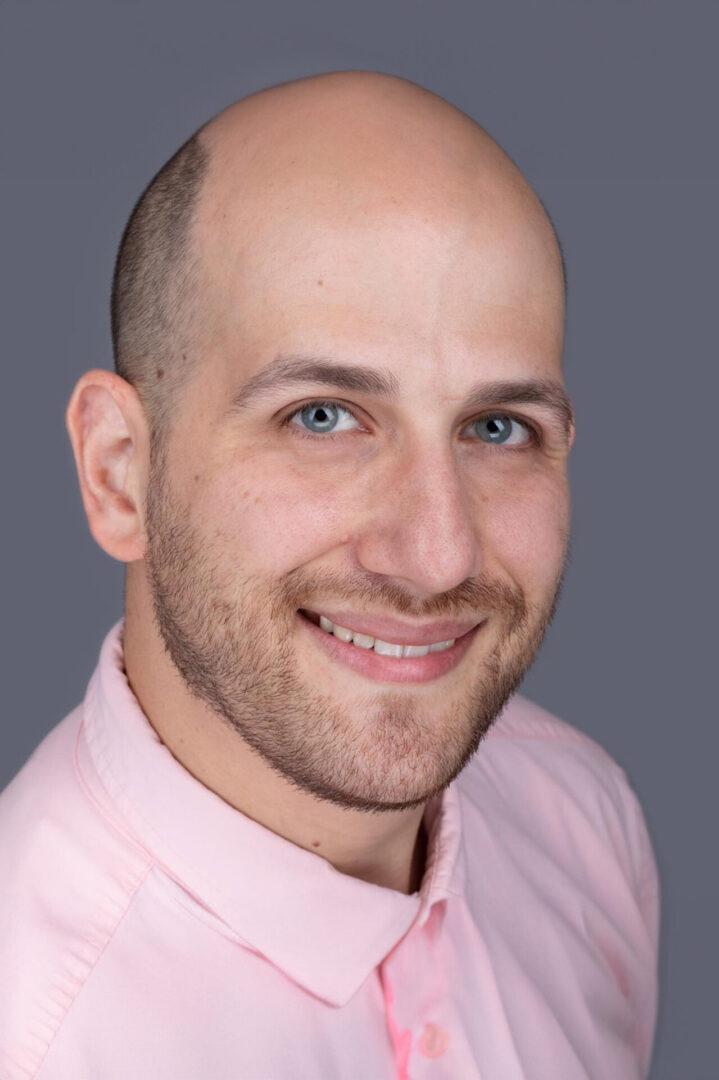 A man with bald head and pink shirt smiling.