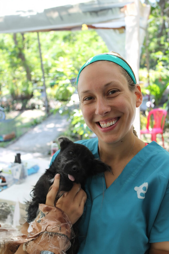 A woman holding a small black dog in her arms.